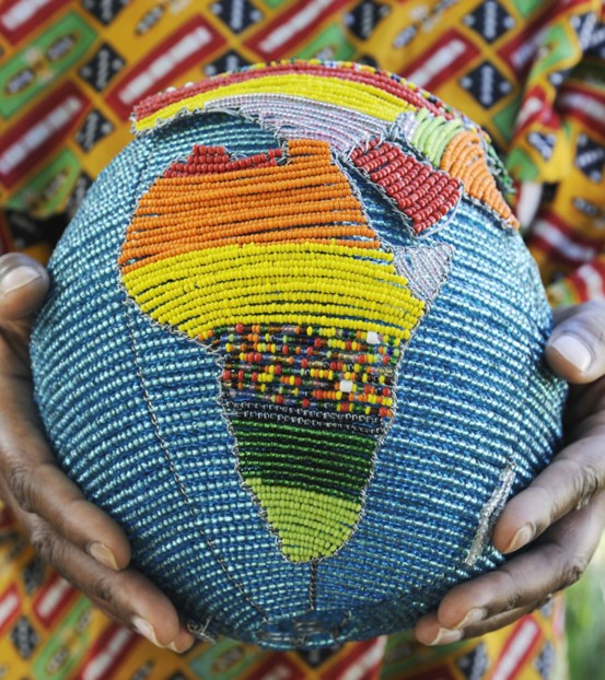 Picture of a beaded handmade globe focusing on Africa with an African person dressed in traditional clothing in the background holding the globe