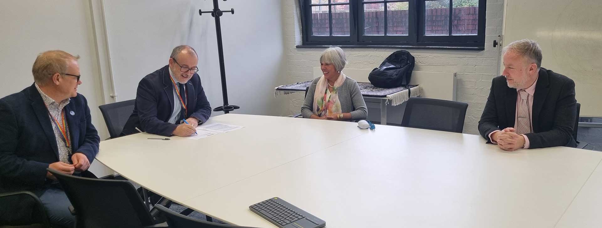 Four people sitting at a table with one signing a document