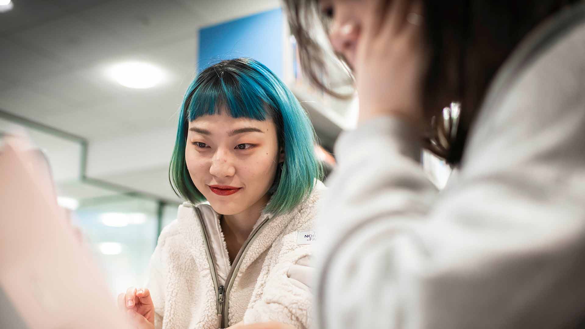 Young student with green hair talking to another female colleague