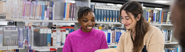 two students looking at a book in the library