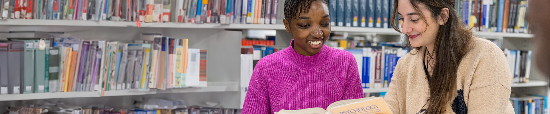 Two international students smiling reading a book in a library