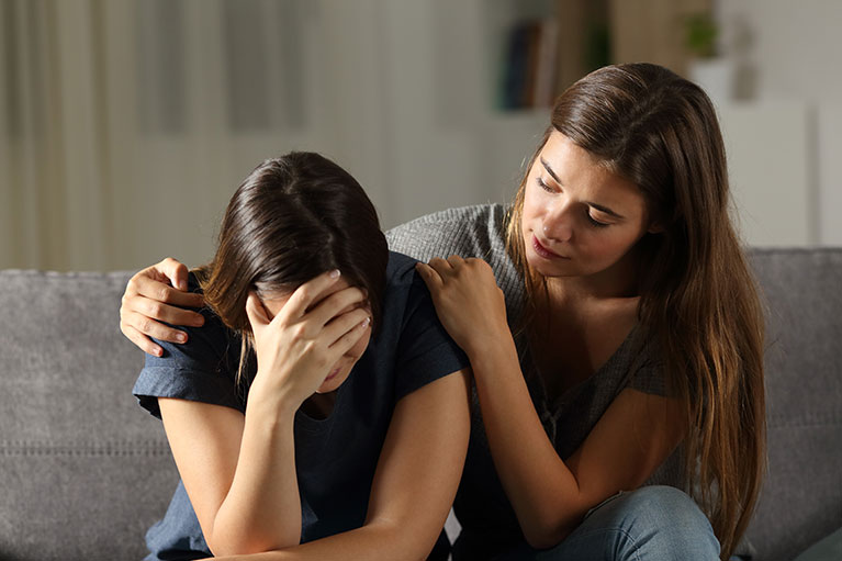 woman comforting another woman sat on the couch