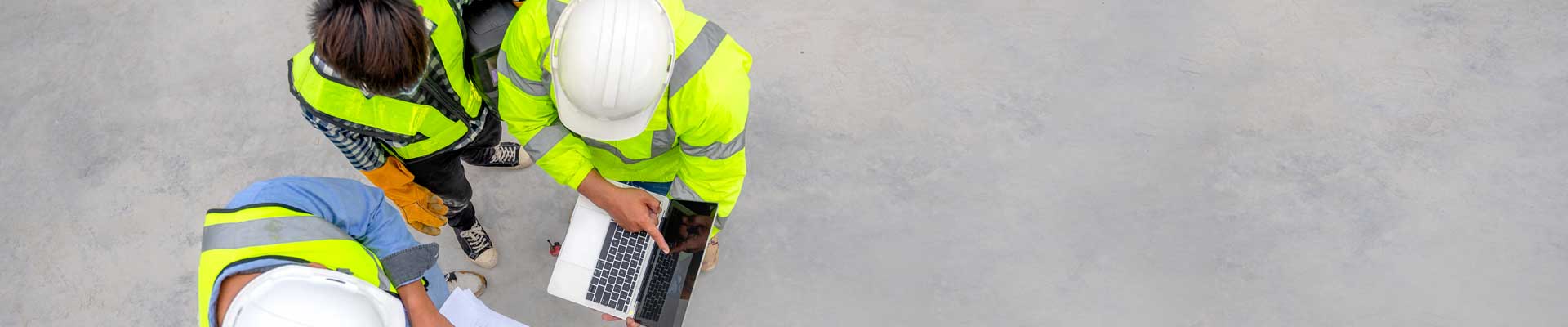 three men wearing yellow vests and hard hats looking over construction plans