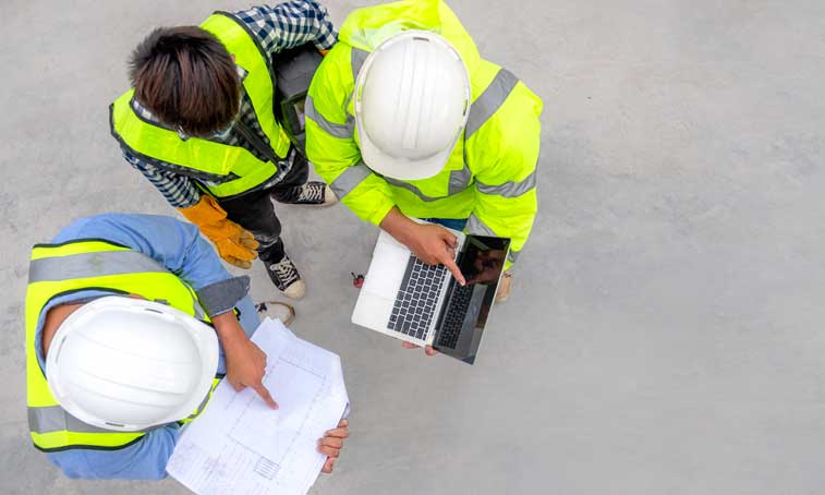 three men wearing yellow vests and hard hats looking over construction plans