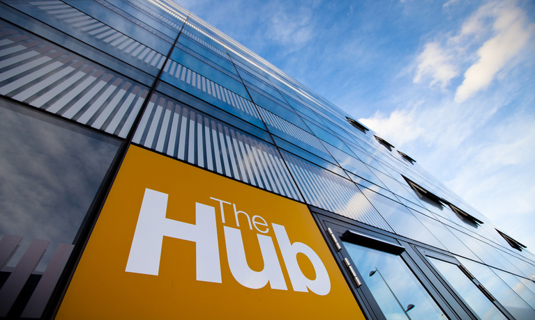 The Hub building from a worms eye view showing The Hub Orange sign glass windows and the sky