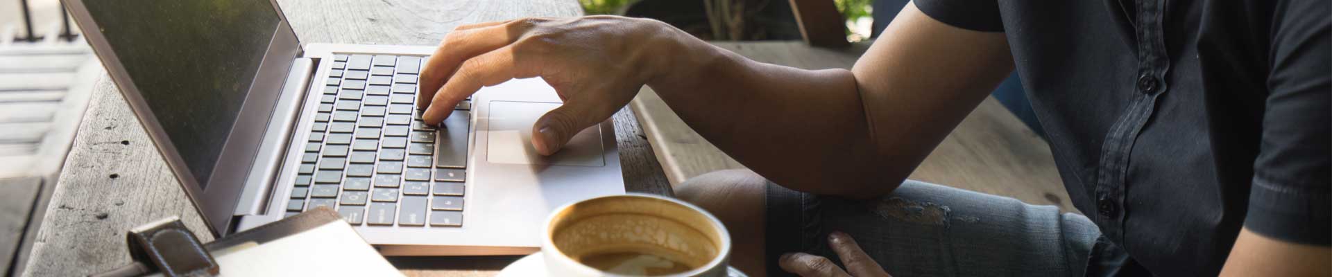 creative freelancer working from the remote location on a laptop with a notebook and a cup of coffee on the side
