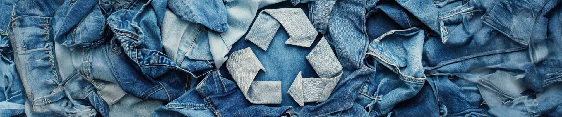 recycle symbol made of denim material on top of pile of discarded jeans