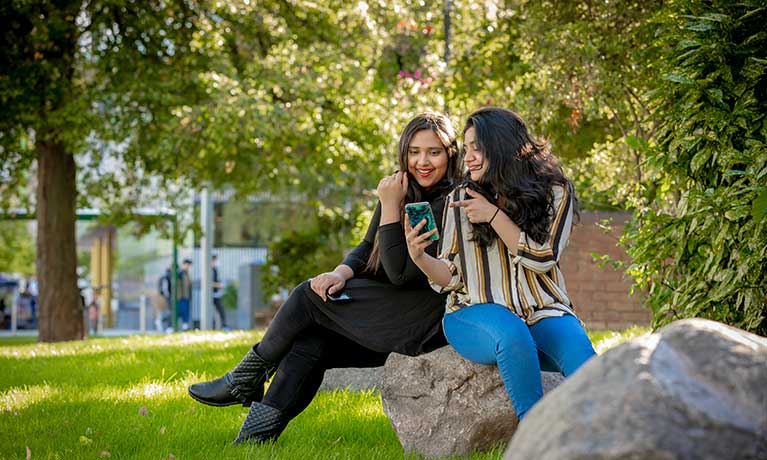 Two students sitting outside on campus looking at a mobile 