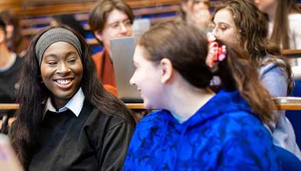 two female students in a lecture theatre chatting 