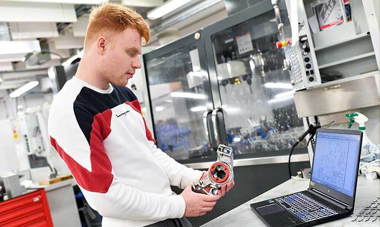 Ali Haddow Motorsport Engineering working on a component with a laptop on the desk in front of him 