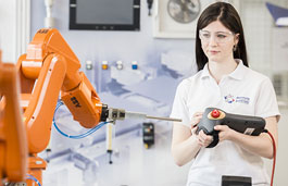 A student in a Manufacturing Engineering lab using the controller for the equipment and wearing safety glasses