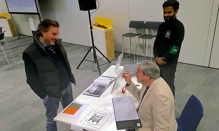 Lecturer at a table chatting to two students 