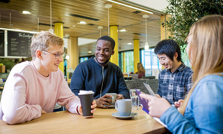 Diverse group of young people sitting at a table having cups of coffee in front of them