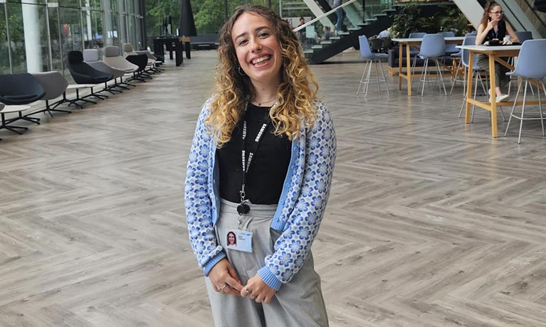 Student sat in large open plan room smiling at the camera