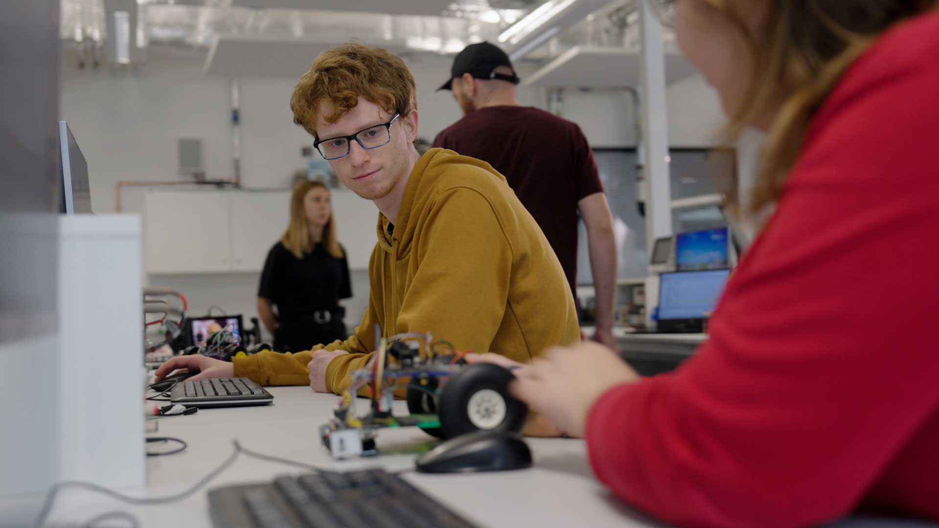 Two students working with a small robot between them, connected to their computers