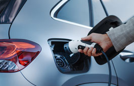 Hand holding an ev charger reaches to put it into a port on a car
