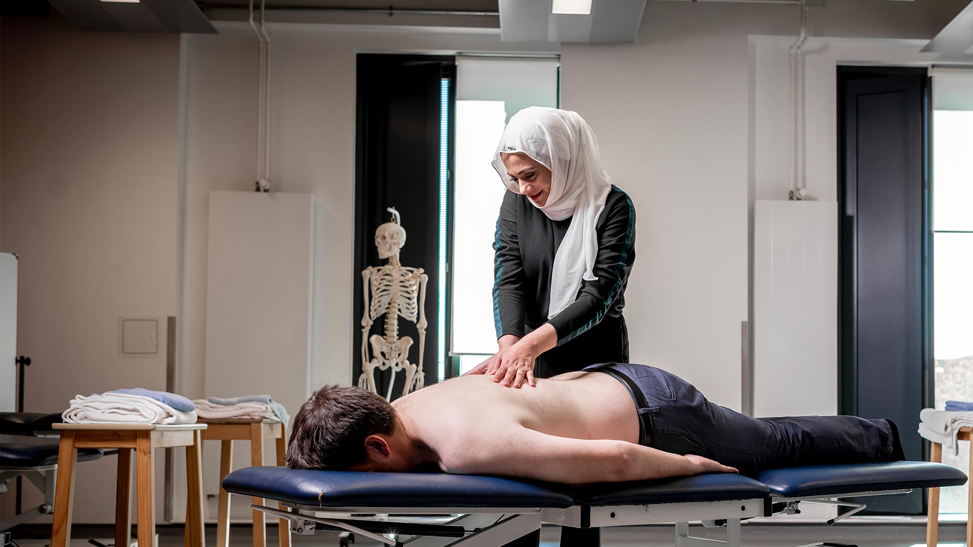 Female giving a back massage to a person lying on a massage bed