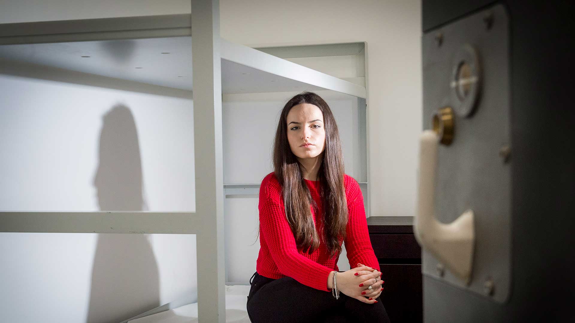 Female sat on a bunk bed inside a cell with the door slightly open