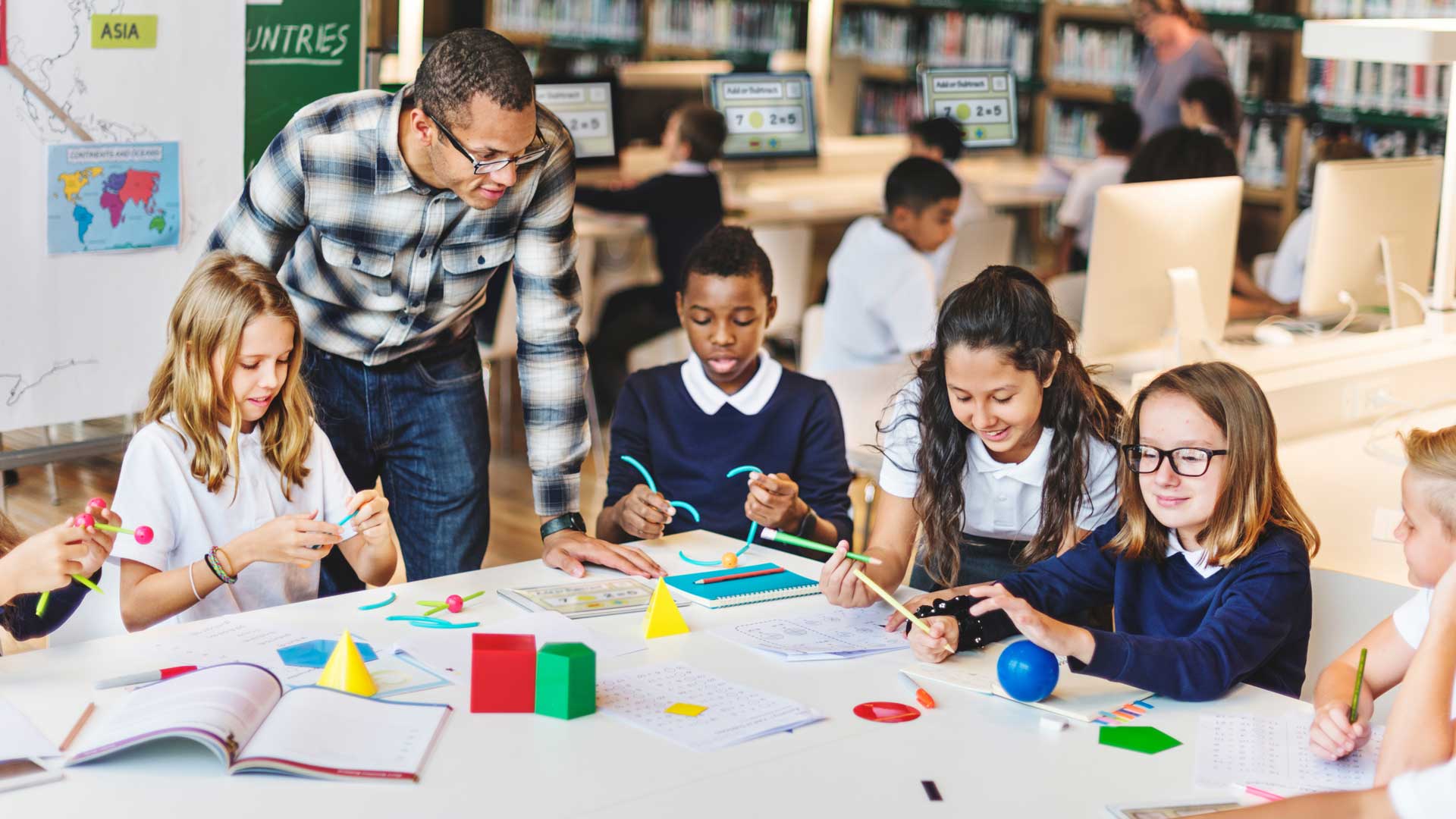 A teacher and students in the classroom sat around a large table, with materials in front of them