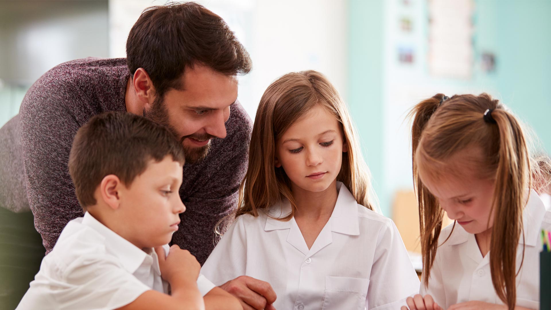A teacher helping young schoolchildren with their reading.