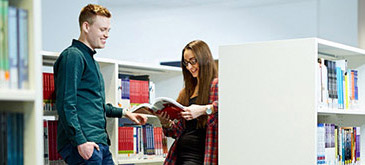 students looking through books in a library aisle
