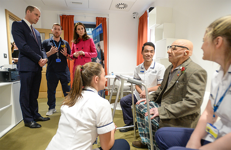 The Duke and Duchess of Cambridge talking to a member of staff whilst students are practicing on a elderly model