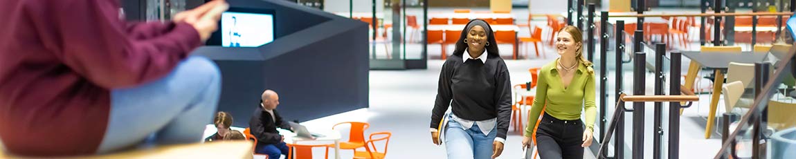 2 female graduates walking up stairs in large open atrium