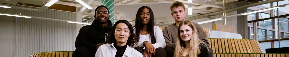 Five students sitting on a raised wooden platform in a inside place