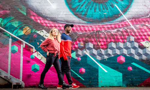 Two students walking past brightly coloured street art in Fargo Village in Coventry.