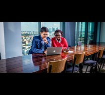 man in a suit sitting with a woman looking at laptop