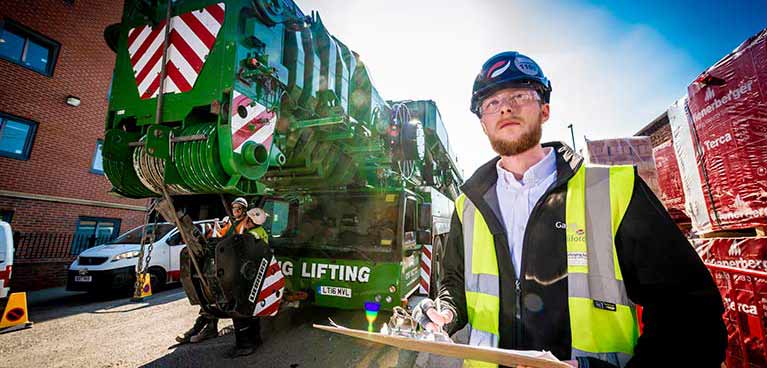 A male construction student with a hard hat one and a clipboard in hand