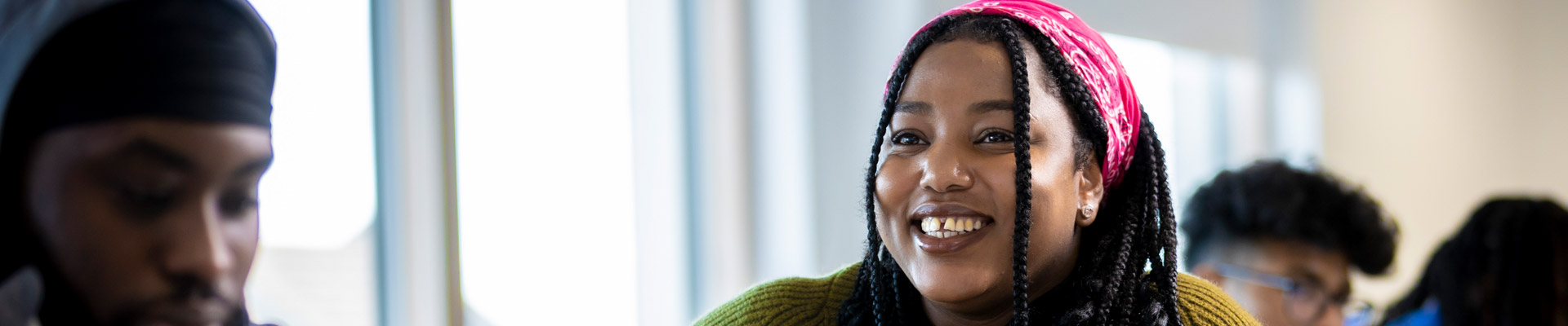 A student wearing a bright pink headscarf smiling while using a laptop in a classroom.