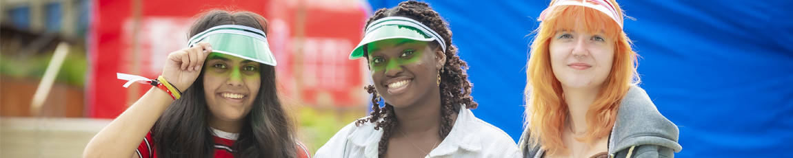 Three students sat outside during Coventry University's welcome week, wearing colourful visors.