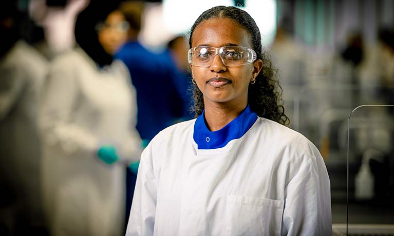 Student in lab coat looking at camera