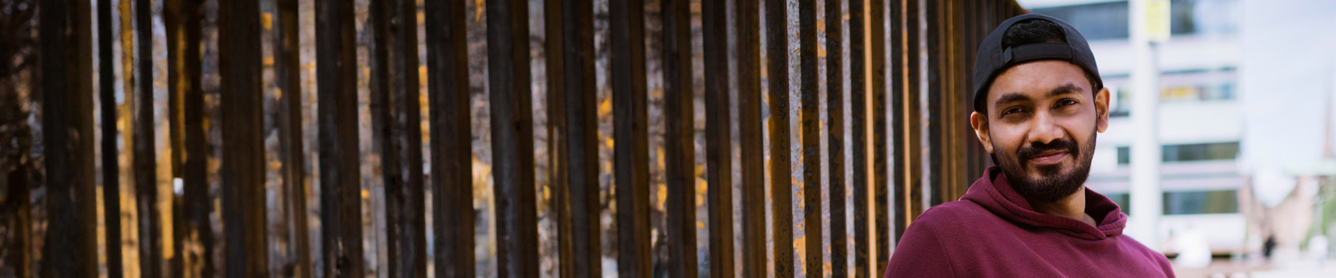 A male student leaning against a wall and smiling at the camera.
