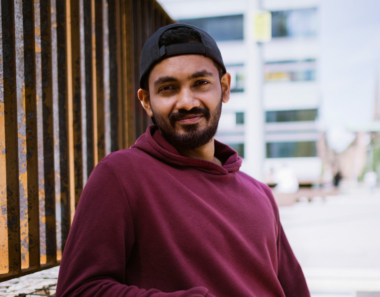 A male student leaning against a wall and smiling at the camera.