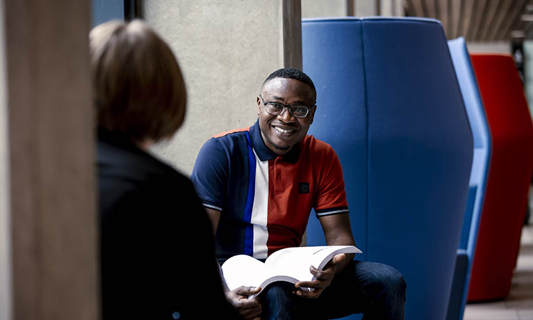 Male student sat in a pod smiling and talking.