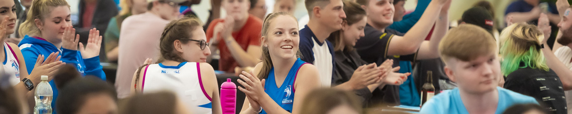 A group of students in Sport Coventry uniforms clapping and cheering at an event.