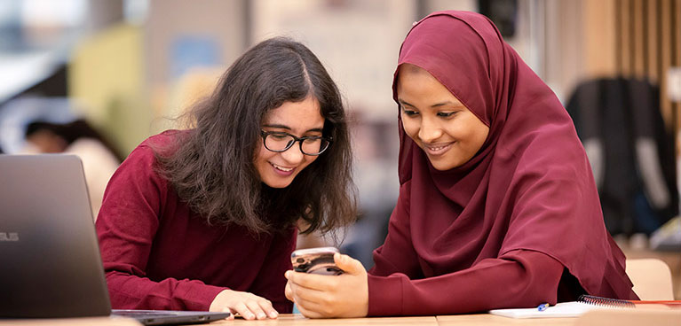 Two students leaning together looking at a phone screen