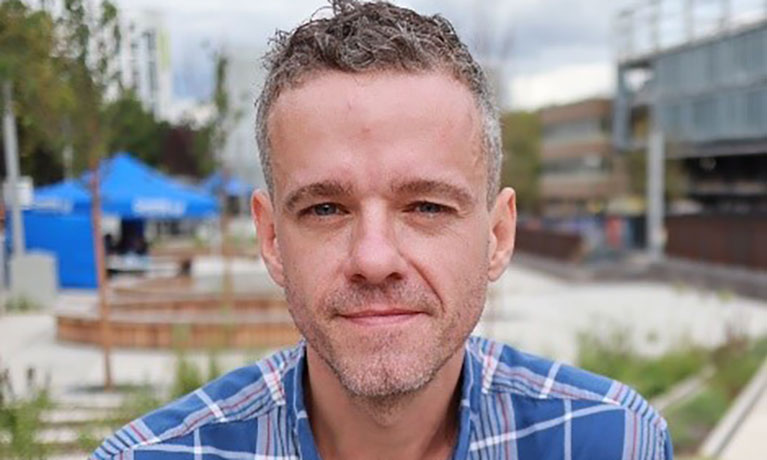 A head and shoulders shot of Dr Marcus Maloney who is wearing a checkered shirt