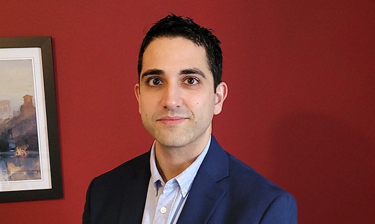 Man wearing a blue suit sitting in front of a red wall