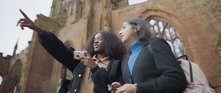 Two students stood outside the cathedral ruins pointing at something in the distance