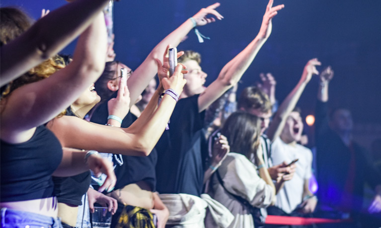 Students with their hands in the air at a music concert.