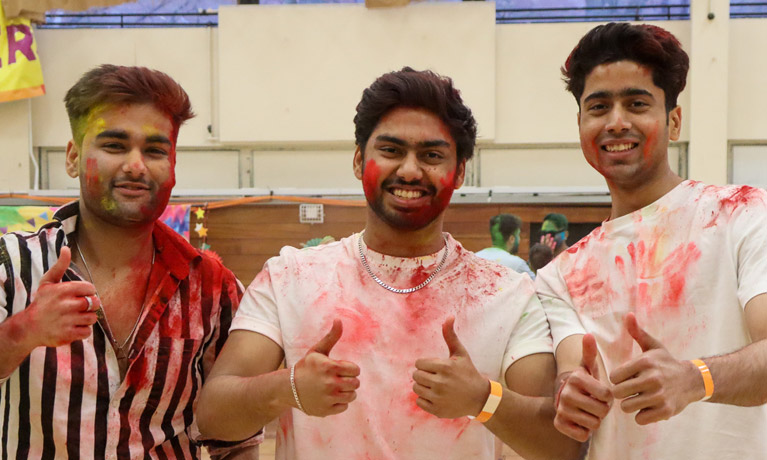Three students covered in coloured powder for a festival as part of a society.