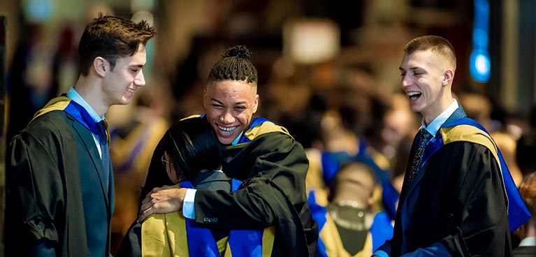 Three young male students smiling while wearing graduation clothing