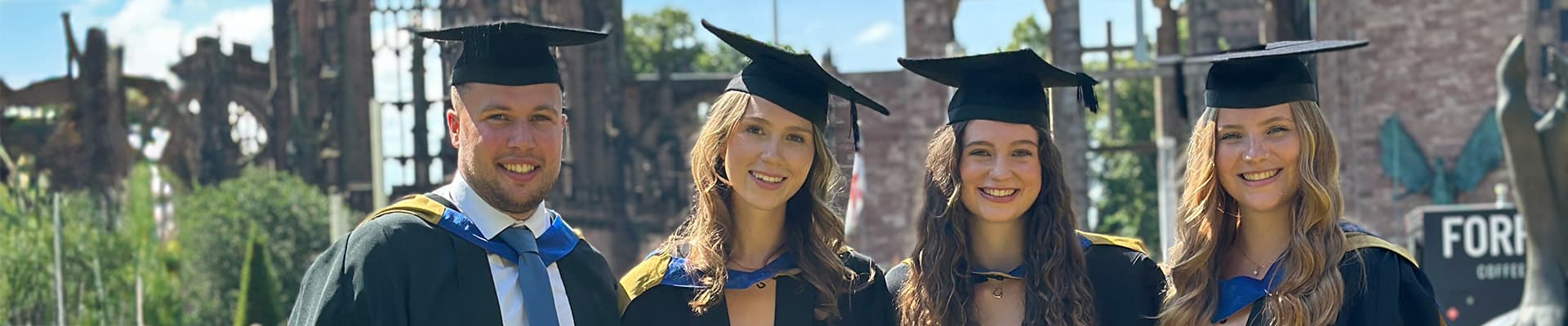 Four graduates stood together smiling on a sunny day