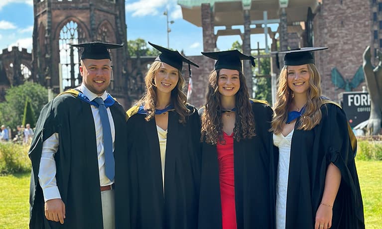 Four graduates stood in front of Coventry Cathedral