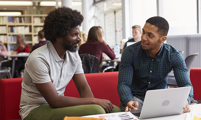 Two men sitting at a table looking at the laptop and talking