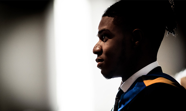 A Black man wearing a graduatation gown and mortar board