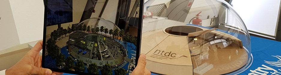 a man's hands hold a tablet which is taking a photograph of a model urban airport